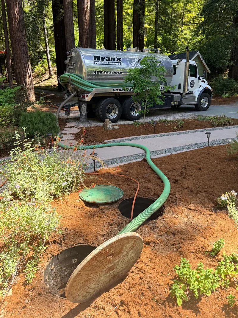 Ryan's truck parked among redwoods with a green hose running to two opened septic tank lids in a landscaped yard